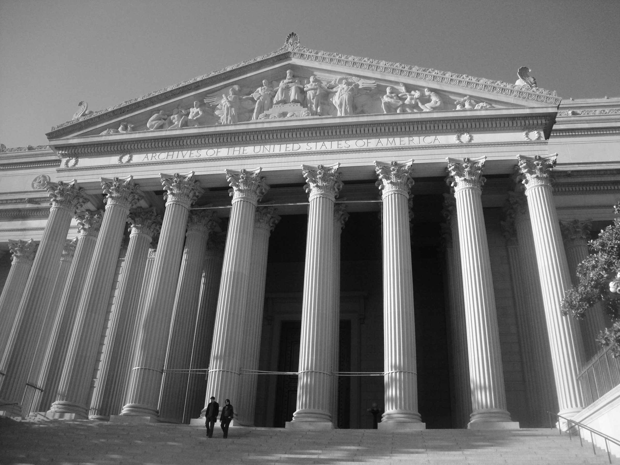 Black and white image looking up at the temple-like facade of the National Archives building in Washington, DC.